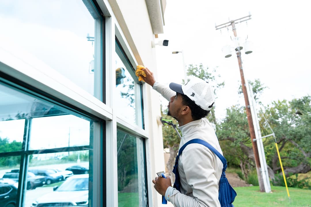 Man cleaning large windows of a commercial building with a cloth and spray bottle.