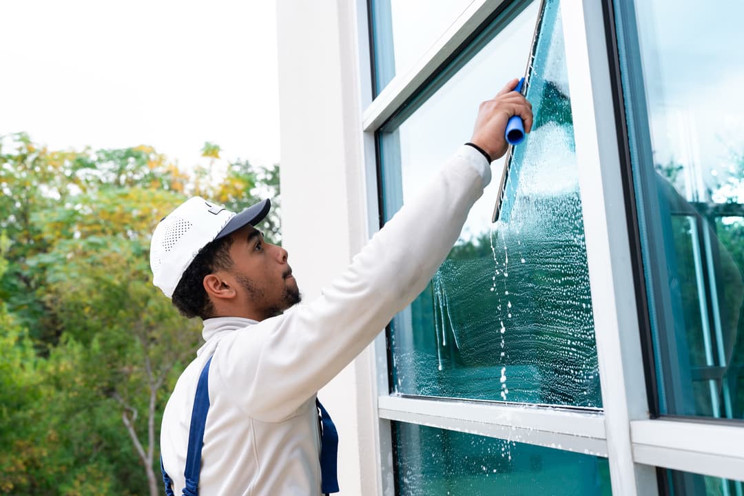 Professional window cleaner using a squeegee on commercial building windows outdoors.