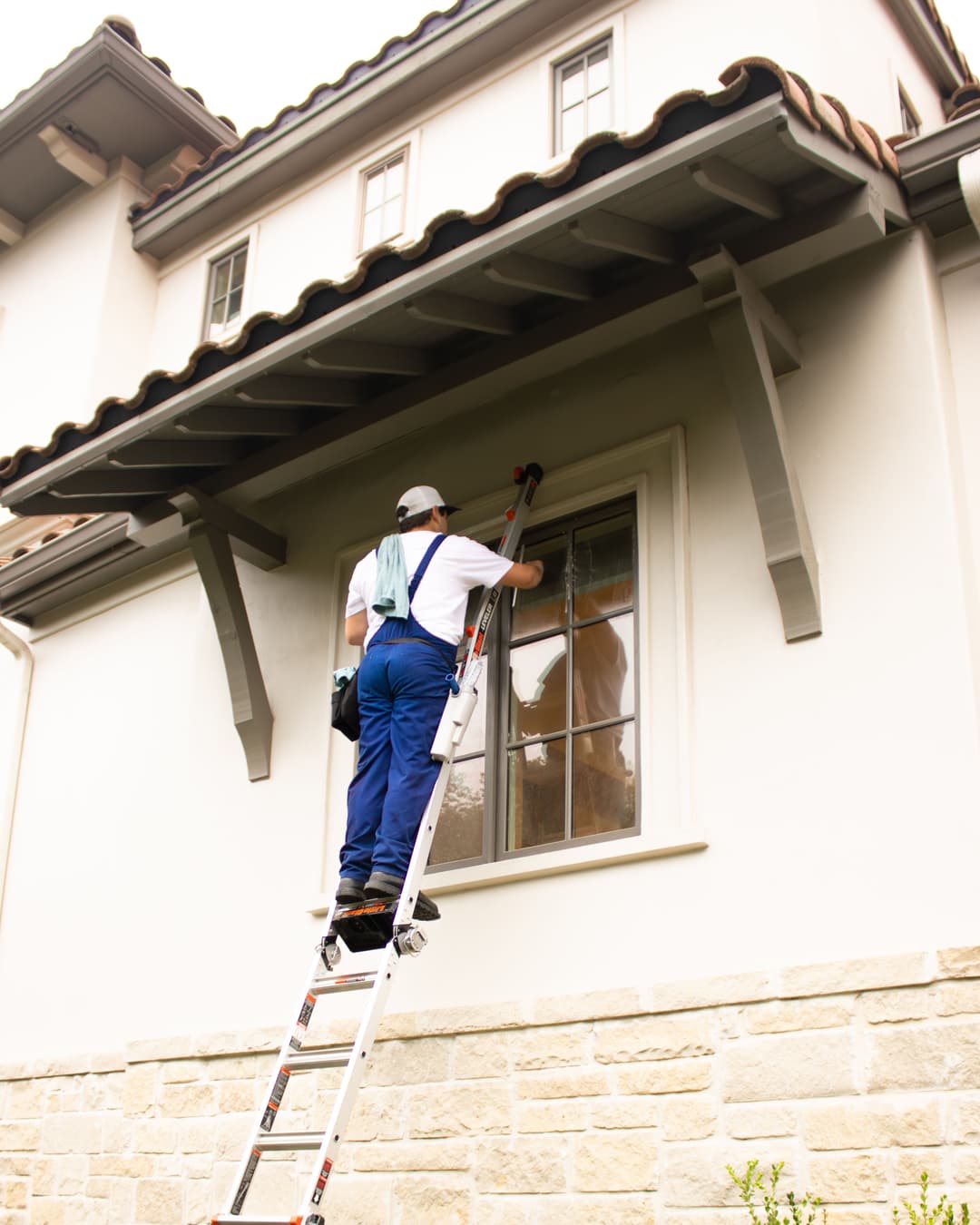 Window cleaning with a ladder on a modern home exterior, highlighting maintenance services.