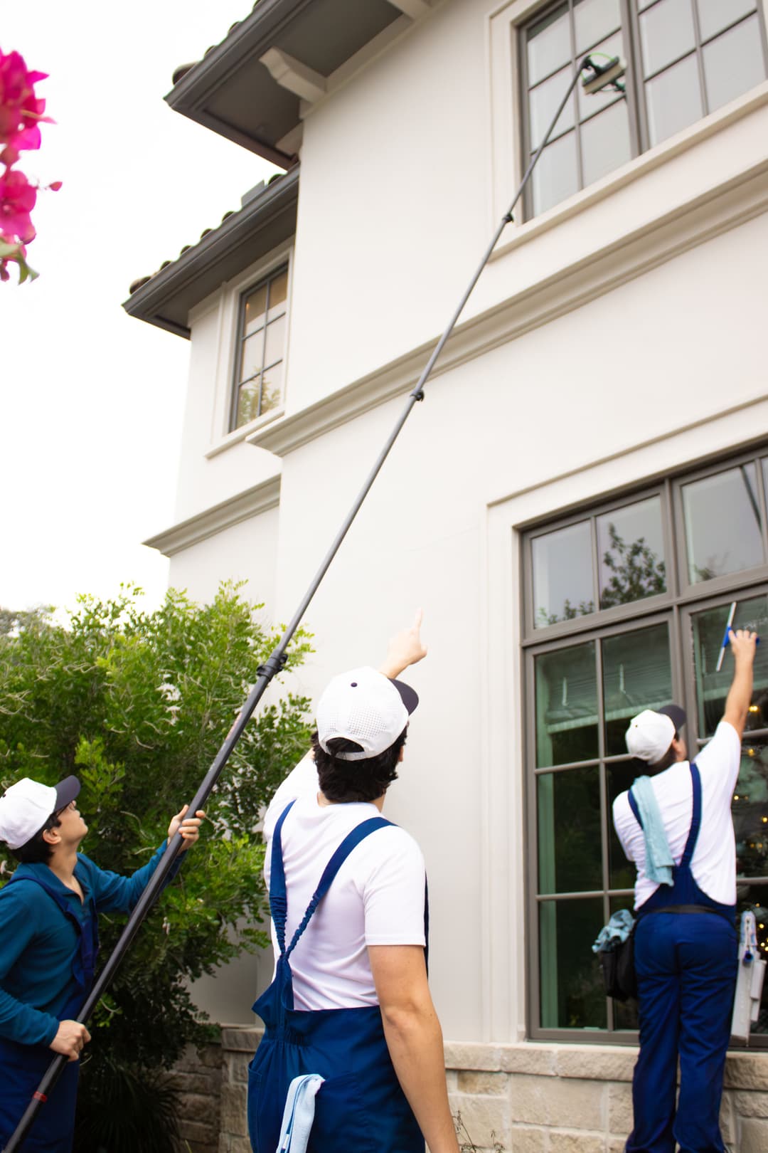 Team of cleaners using equipment to wash windows on a two-story house exterior.