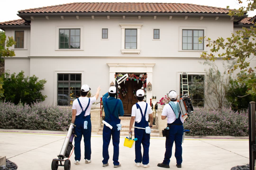 Team of four painters with tools preparing to paint a house exterior.