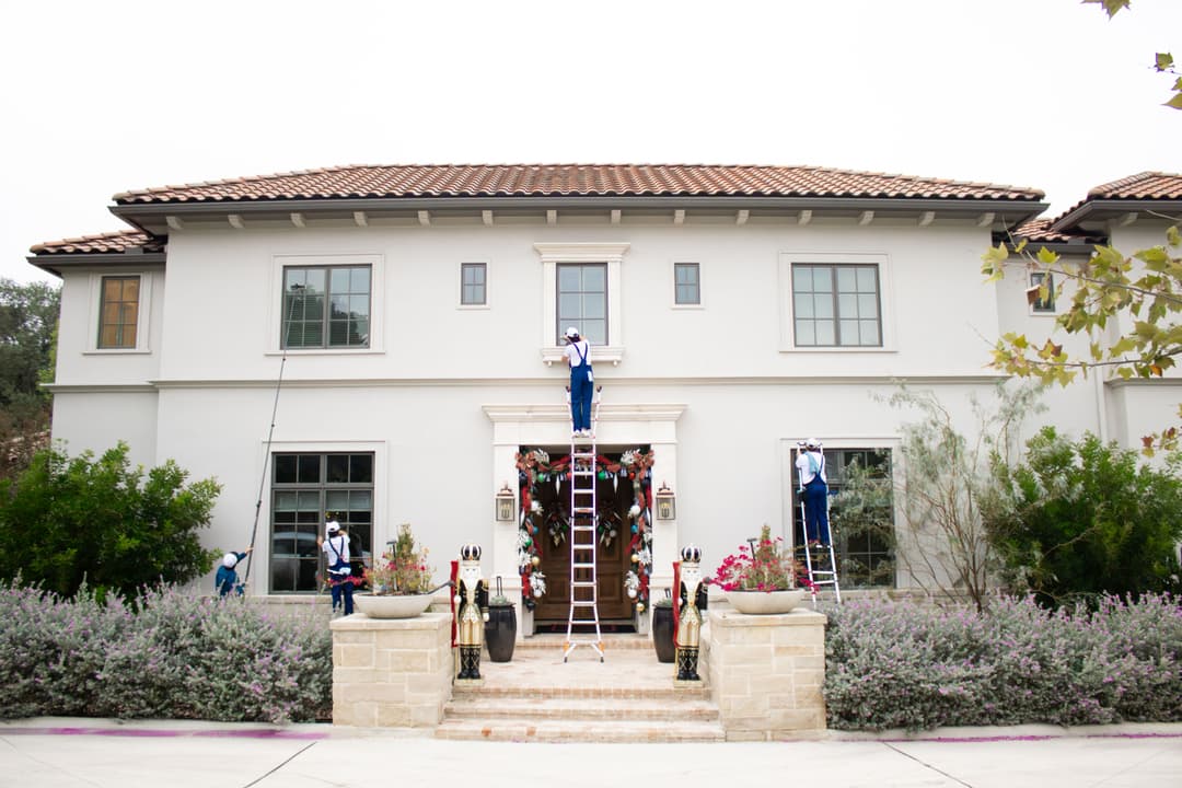 Workers cleaning windows on a luxury home with ladders and scaffolding.
