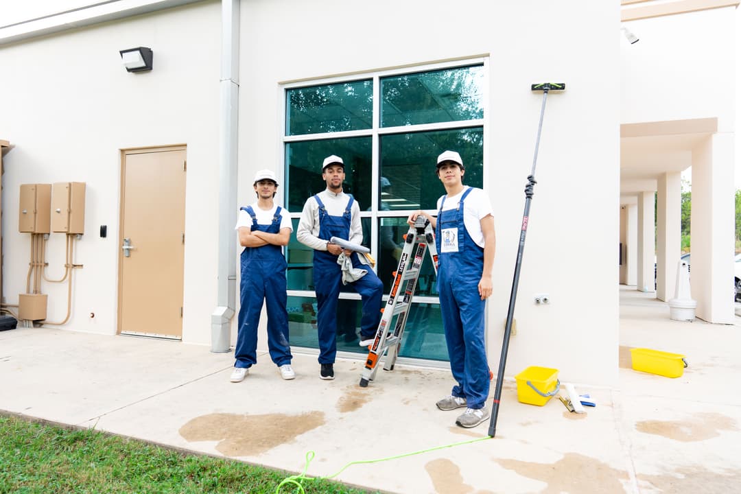Three professional window cleaners in blue coveralls working outside a commercial building.